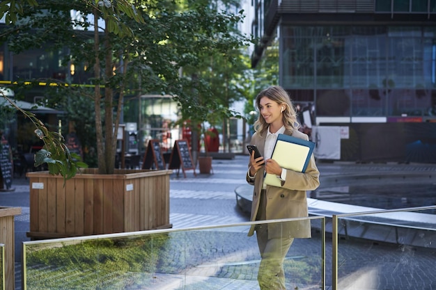 Retrato de mulher corporativa de terno usando telefone celular esperando por parceiro de negócios no centro da cidade h