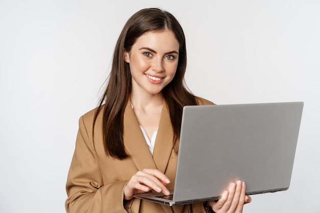 Retrato de mulher corporativa trabalhando com laptop sorrindo e olhando fundo branco assertivo