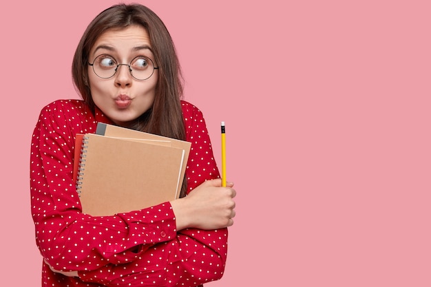 Retrato de mulher de camisa vermelha e óculos redondos segurando blocos de notas