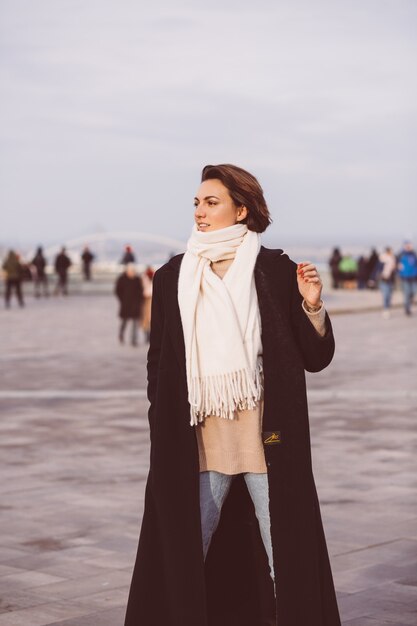 Retrato de mulher de casaco preto de inverno e lenço branco na praça da cidade.