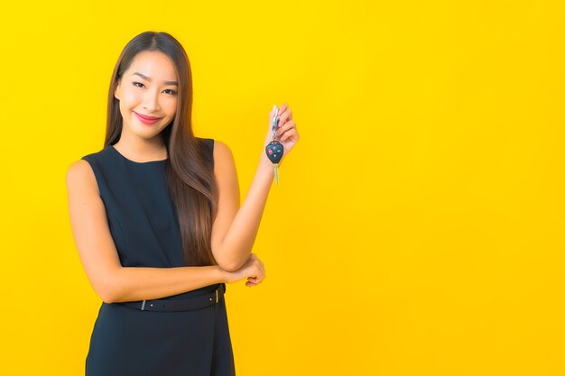 Retrato de mulher de negócios asiática jovem bonita com chave de carro em fundo amarelo.