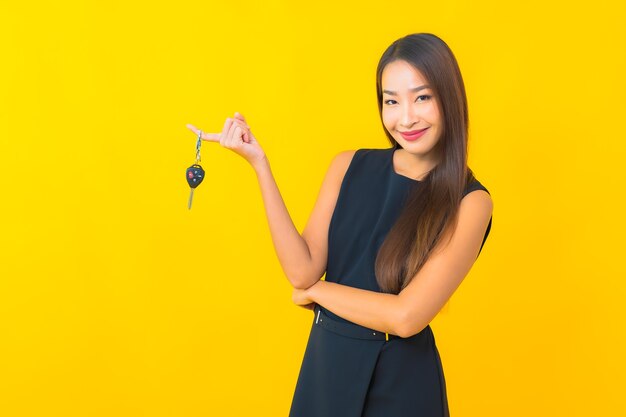 Retrato de mulher de negócios asiática jovem bonita com chave de carro em fundo amarelo.