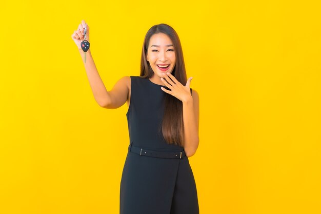 Retrato de mulher de negócios asiática jovem bonita com chave de carro em fundo amarelo.