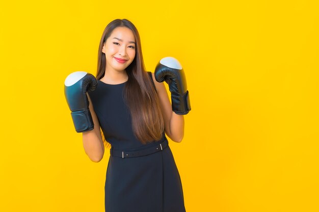 Retrato de mulher de negócios asiática jovem bonita com luva de boxe em fundo amarelo.