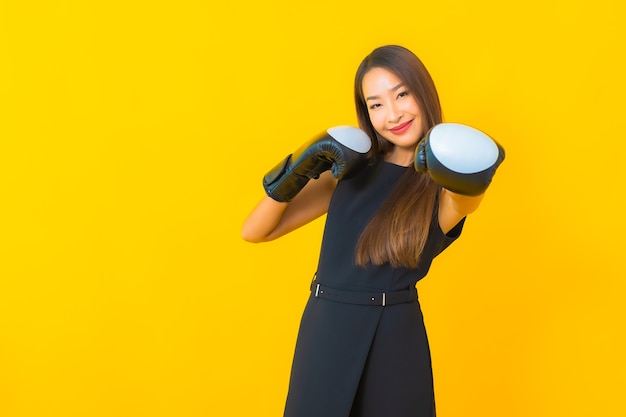 Retrato de mulher de negócios asiática jovem bonita com luva de boxe em fundo amarelo.