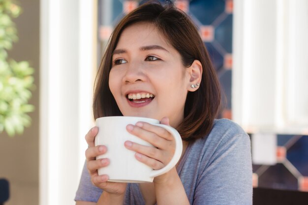 Retrato de mulher de negócios asiáticos jovem feliz com caneca nas mãos bebendo café da manhã