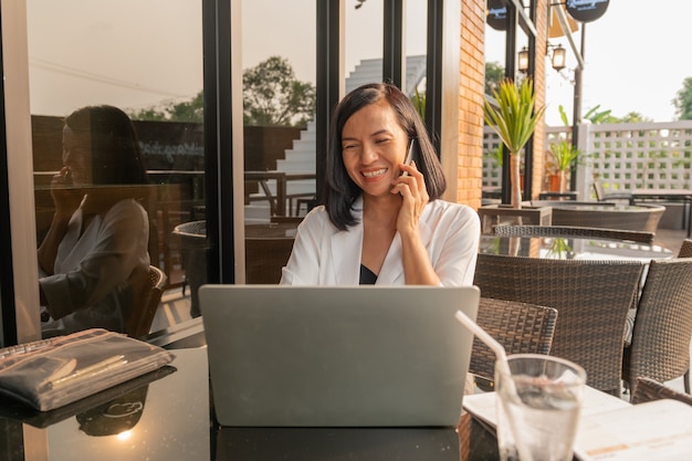 Retrato de mulher de negócios em um café usando um laptop e falando ao celular
