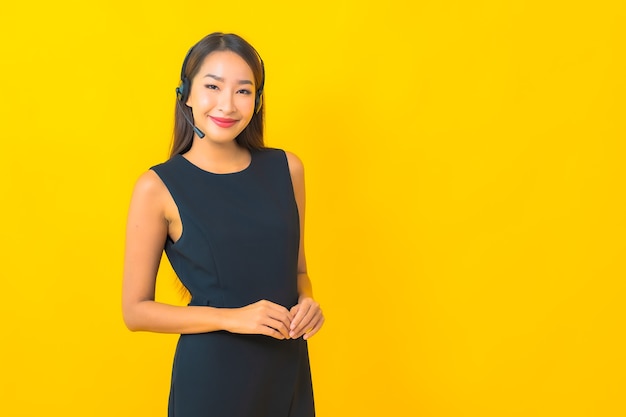 Retrato de mulher de negócios jovem asiática linda com fone de ouvido call center atendimento ao cliente em fundo amarelo Foto gratuita