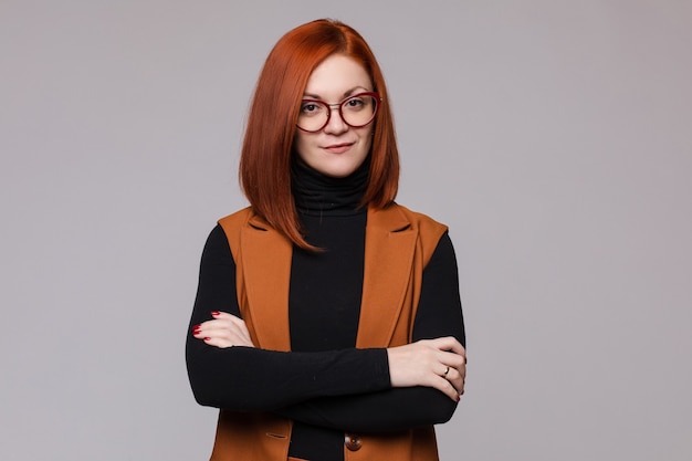 Retrato de mulher de negócios ruiva sorridente em copos posando olhando para a câmera de tiro médio. beleza feminina chefe europeia em pé com a mão cruzada isolada no fundo branco do estúdio