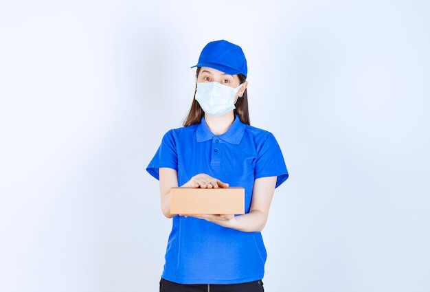 Retrato de mulher de uniforme e máscara médica segurando uma caixa de papel