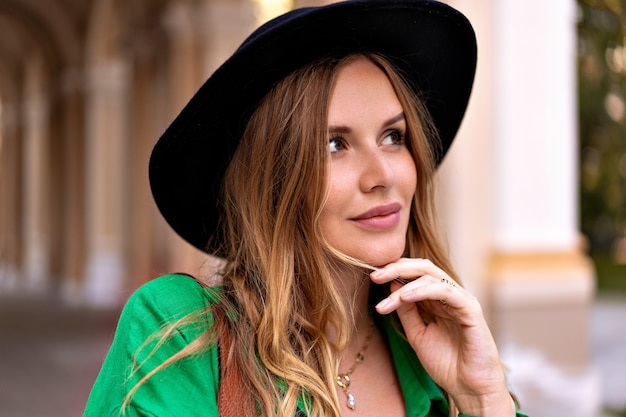 retrato de mulher elegante e elegante com cabelo loiro encaracolado rosto sardento e maquiagem natural, usando fedora preto posando na rua.