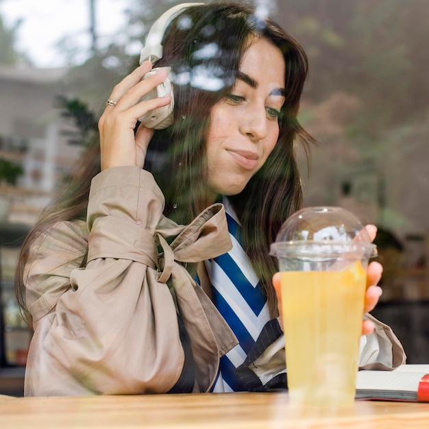 Foto grátis retrato de mulher em um café com limonada fresca e fones de ouvido