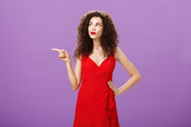 Retrato de mulher encantadora pensativa e sonhadora com penteado encaracolado em elegante vestido de noite vermelho p.