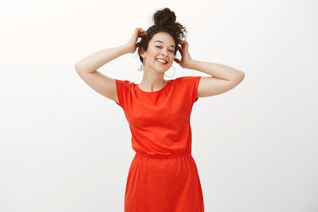 Retrato de mulher europeia confiante e despreocupada, com cabelo cacheado penteado, segurando as mãos na cabeça e sorrindo positivamente