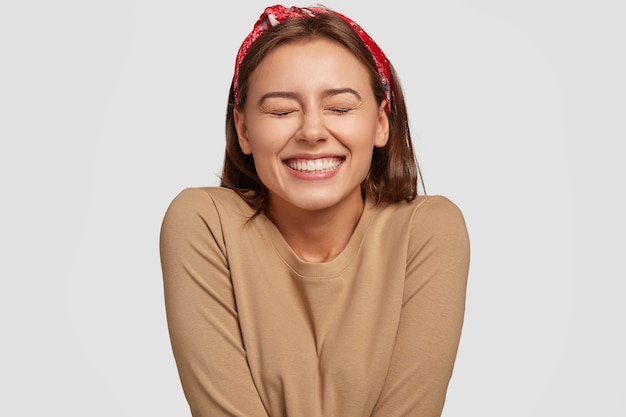 Retrato de mulher européia feliz com sorriso largo, fecha os olhos, sente empolgação, está em alta