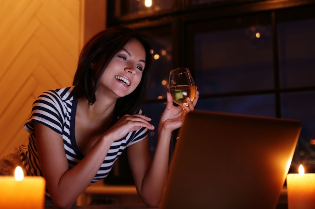retrato de mulher feliz com um copo de vinho, olhando para a tela do pc