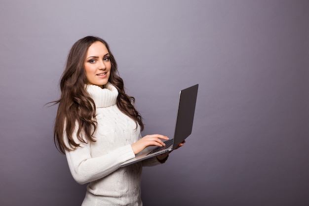 Retrato de mulher feliz e surpresa em pé com laptop isolado na parede cinza