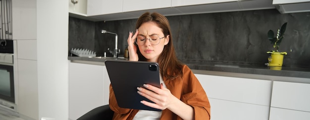 Retrato de mulher freelancer usando óculos segurando tablet digital parecendo cansada tem enxaqueca ou