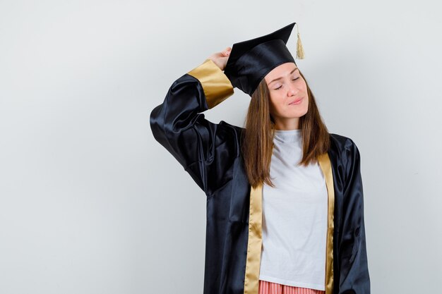 Retrato de mulher graduada posando com a mão levantada na cabeça em uniforme, roupas casuais e uma vista frontal encantadora