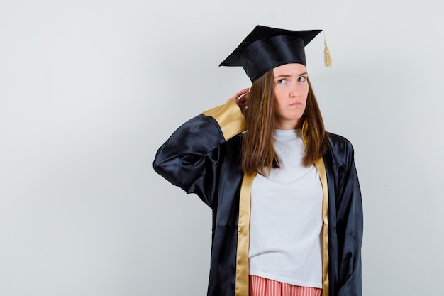 Retrato de mulher graduada segurando a mão atrás da cabeça em uniforme, roupas casuais e olhando pensativa para a frente