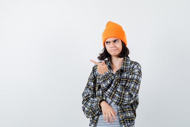 Retrato de mulher jovem apontando para cima com uma camisa quadriculada de chapéu laranja parecendo sombrio