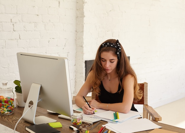 Retrato de mulher jovem atenta, estudando línguas estrangeiras no site da Internet, fazendo anotações em adesivos para memorizar melhor as novas palavras. Copie a parede do espaço para conteúdo ou texto publicitário.