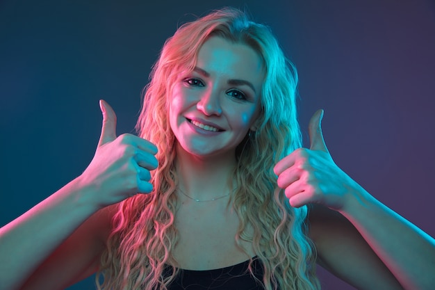 Retrato de mulher jovem caucasiana em fundo gradiente em luz de néon. Bela modelo feminino com aparência incomum. Conceito de emoções humanas, expressão facial, vendas, anúncio. Apontando, sorrindo. Copyspace.