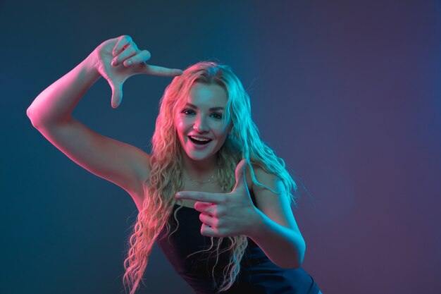 Retrato de mulher jovem caucasiana em fundo gradiente em luz de néon. Bela modelo feminino com aparência incomum. Conceito de emoções humanas, expressão facial, vendas, anúncio. Sorrindo fofo.