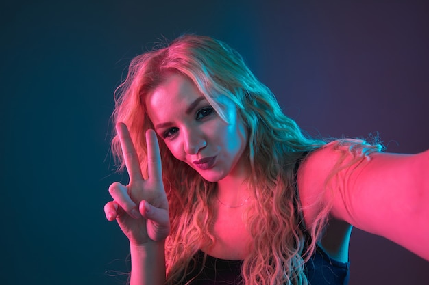 Retrato de mulher jovem caucasiana em fundo gradiente em luz de néon. Linda modelo feminino com aparência incomum. Conceito de emoções humanas, expressão facial, vendas, anúncio. Fazendo selfie, posando.