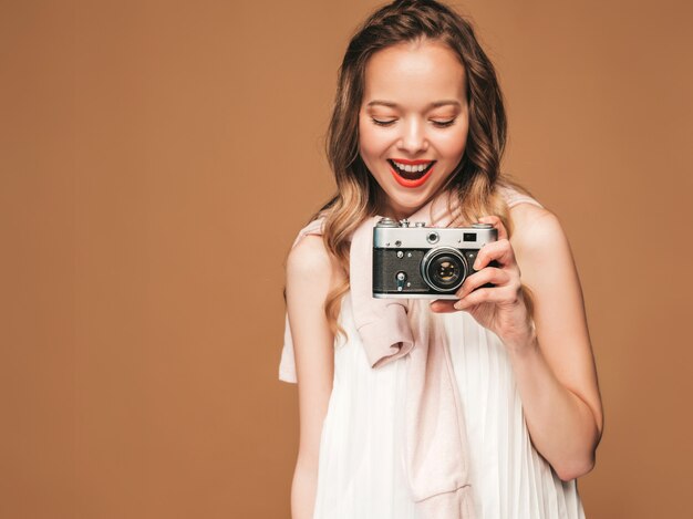 Retrato de mulher jovem e alegre, tirando foto com inspiração e usando vestido branco. Menina segurando a câmera retro. Levantamento modelo