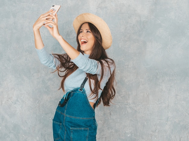 Retrato de mulher jovem e alegre, tirando foto de selfie com inspiração e usando chapéu e roupas modernas.