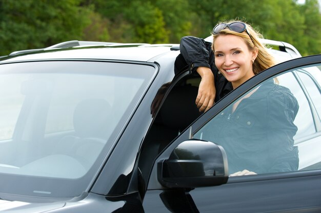 Retrato de mulher jovem e atraente feliz no novo carro - ao ar livre