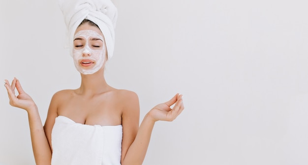 Retrato de mulher jovem e bonita com toalhas após o banho fazer máscara cosmética no rosto.