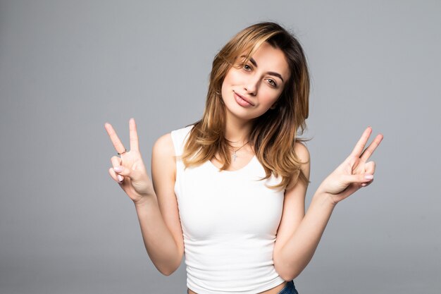 Retrato de mulher jovem e bonita mostrando dois dedos ou gesto de vitória, na parede cinza, com área em branco copyspace para texto ou slogan