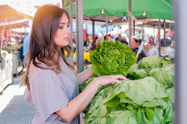 Retrato de mulher jovem e bonita que escolhe vegetais de folhas verdes no mercado verde. Conceito de compras de alimentos saudáveis. Jovem comprando vegetais no mercado verde.