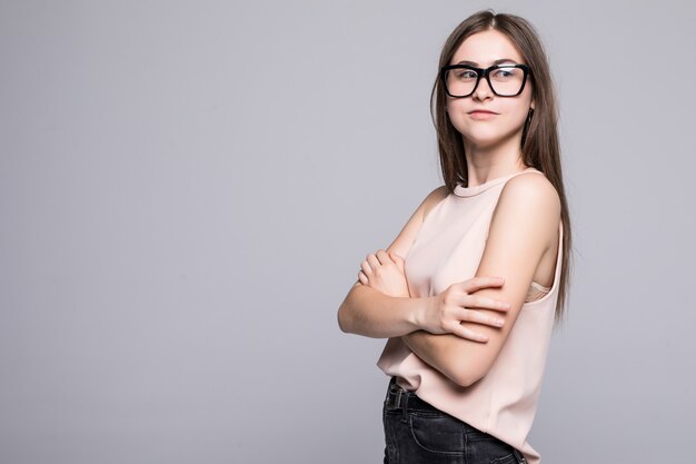 Retrato de mulher jovem e bonita sorrindo, em pé com os braços cruzados sobre parede branca