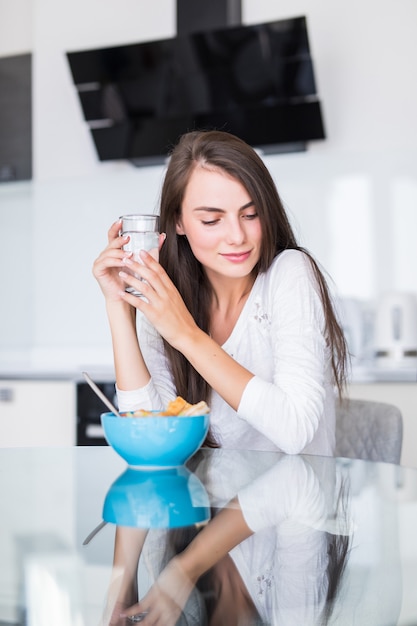 Retrato de mulher jovem e bonita tomando café na cozinha.