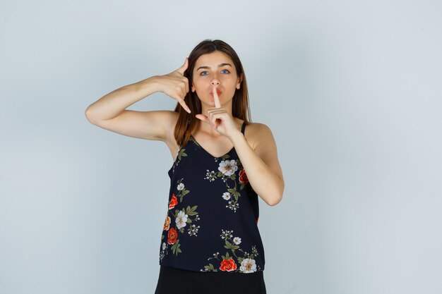 Retrato de mulher jovem mostrando gesto de telefone e sinal de silêncio na blusa, saia e olhando a vista frontal cuidadosa