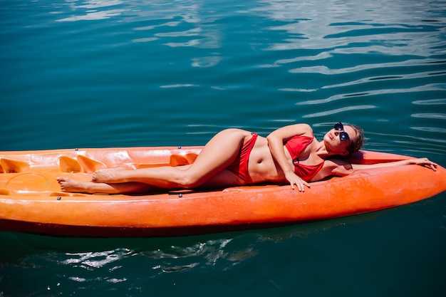 Retrato de mulher jovem turista caucasiano apto em biquíni relaxante em caiaque no belo lago na Tailândia. Mulher de férias aproveitando o dia de sol.