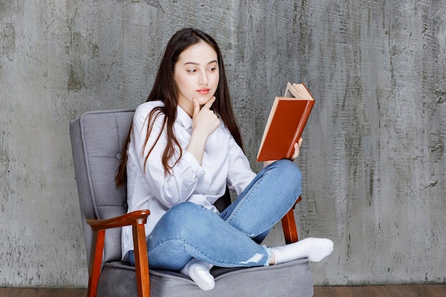 Retrato de mulher lendo livro enquanto está sentado na poltrona. Foto de alta qualidade