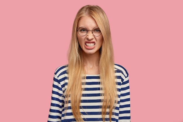 Retrato de mulher loira irritada posando contra a parede rosa