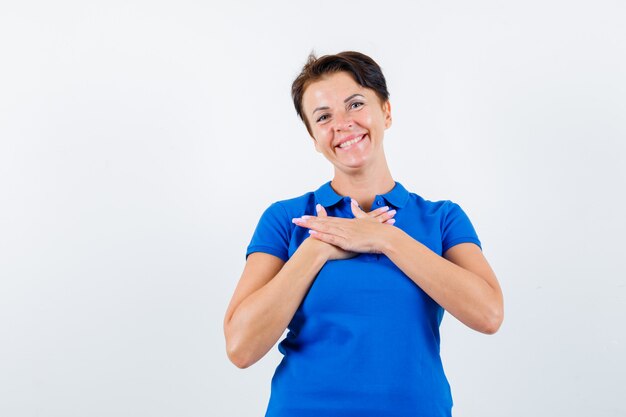 Retrato de mulher madura de mãos dadas no peito em uma camiseta azul e olhando frontalmente feliz