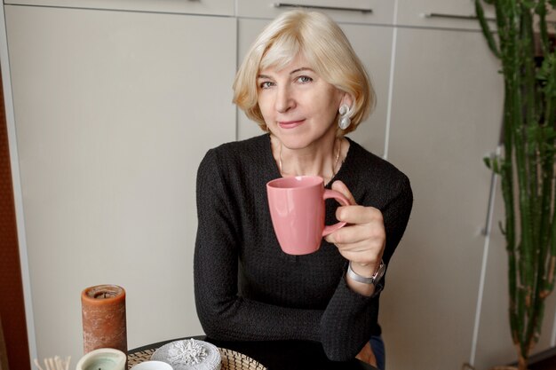 Retrato de mulher madura saudável magro bonita com uma xícara de café posando em sua cozinha moderna