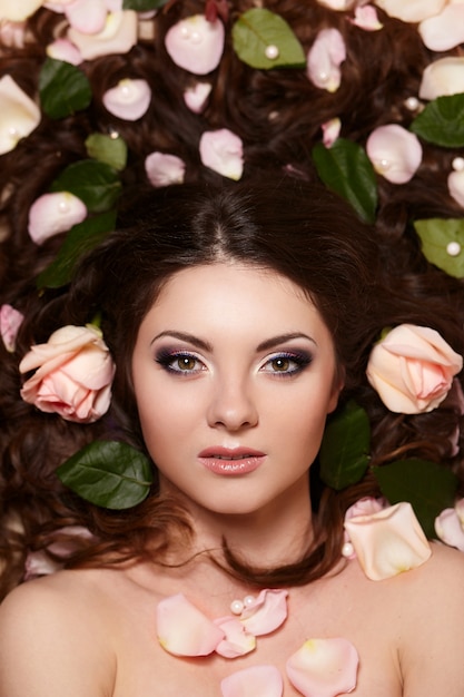 Foto grátis retrato de mulher morena bonita com cabelo longo cacheado e maquiagem brilhante witjh flores no cabelo