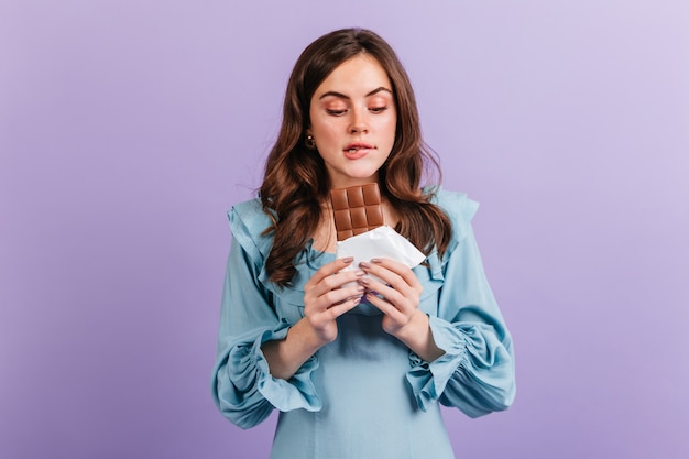 Foto grátis retrato de mulher morena engraçada mordendo o lábio em antecipação ao saboroso almoço. menina de vestido azul parece um delicioso chocolate.