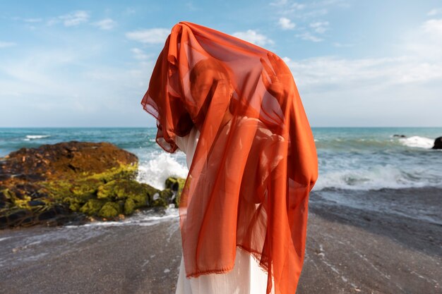 Retrato de mulher na praia cobrindo o rosto com véu