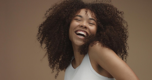 Foto grátis retrato de mulher negra de raça mista com cabelo afro grande e encaracolado em fundo bege riso natural