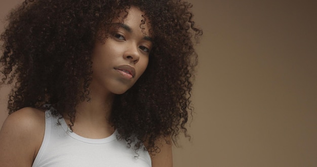 Retrato de mulher negra de raça mista com grande cabelo encaracolado afro em fundo bege