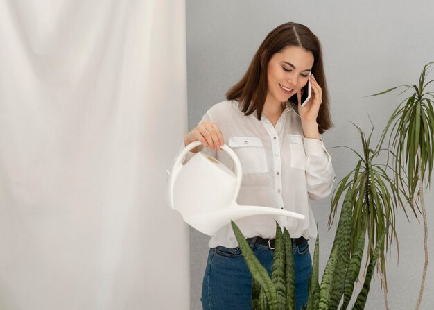 Retrato de mulher regando planta enquanto fala no celular