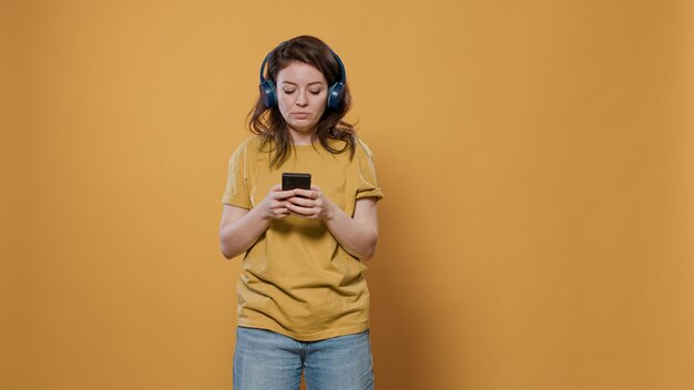Retrato de mulher relaxante usando smartphone ouvindo música em fones de ouvido sem fio começando a dançar no estúdio. Pessoa confiante segurando o celular usando o aplicativo de streaming online para entretenimento.